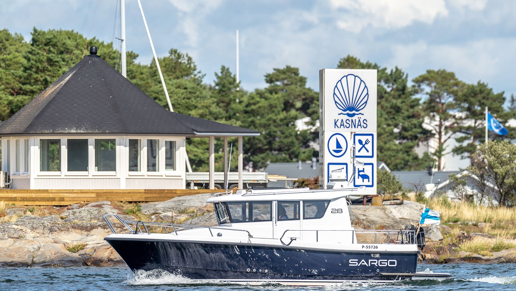 En båt kör förbi en vit byggnad och en stor vit skylt som annonserar Kasnäs Resort.