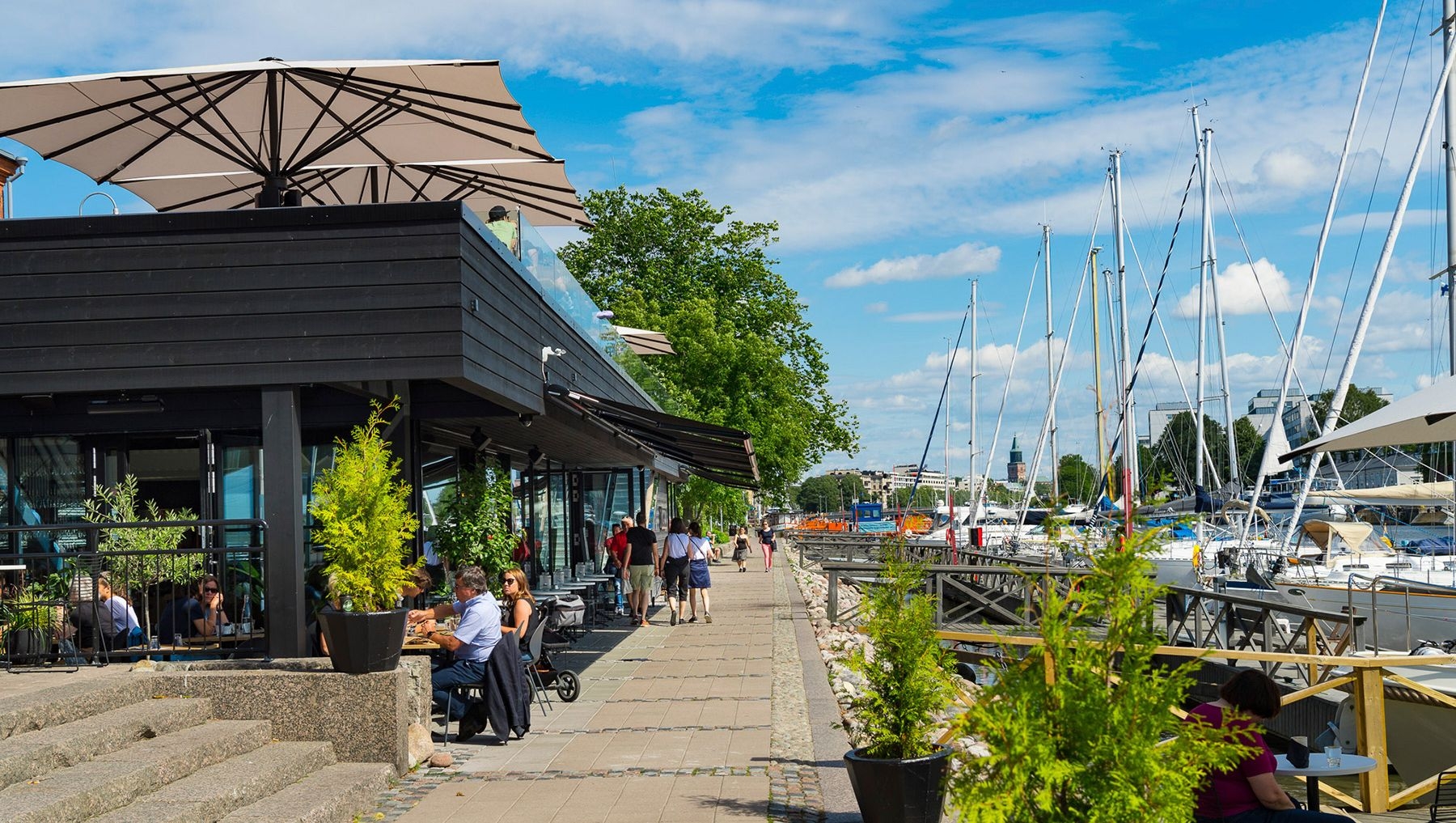Boats line the riverbank at the Turku Guest Harbour, while diners enjoy a meal at NOOA.