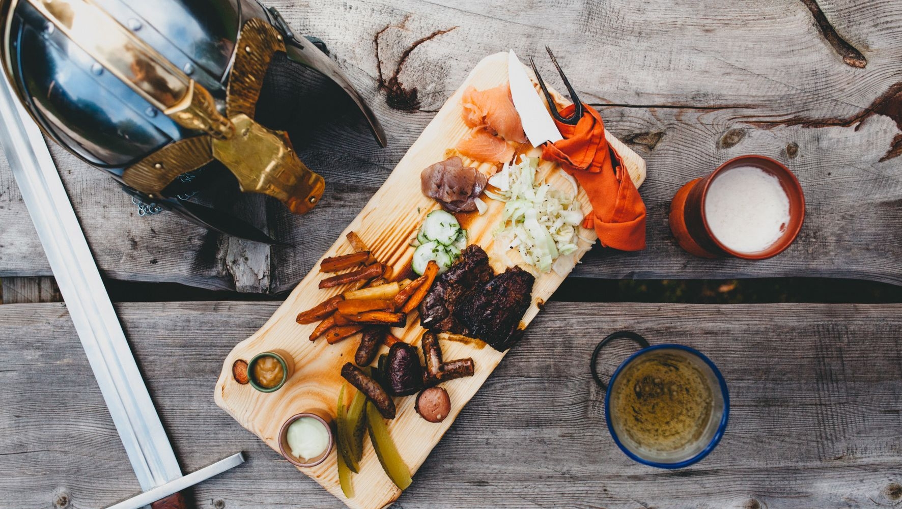 A replica Viking sword and helmet rest beside a wooden platter, filled with different types of delicacies.