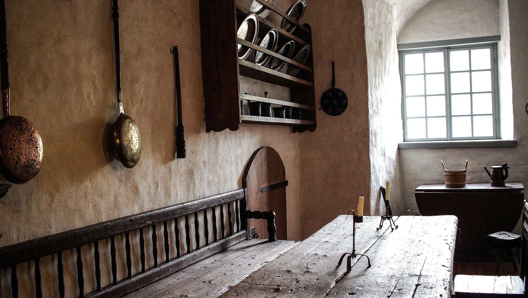 Inredningen i köket på Åbo slott, med ett långt träbord och kastruller och stekpannor hängande på väggen.