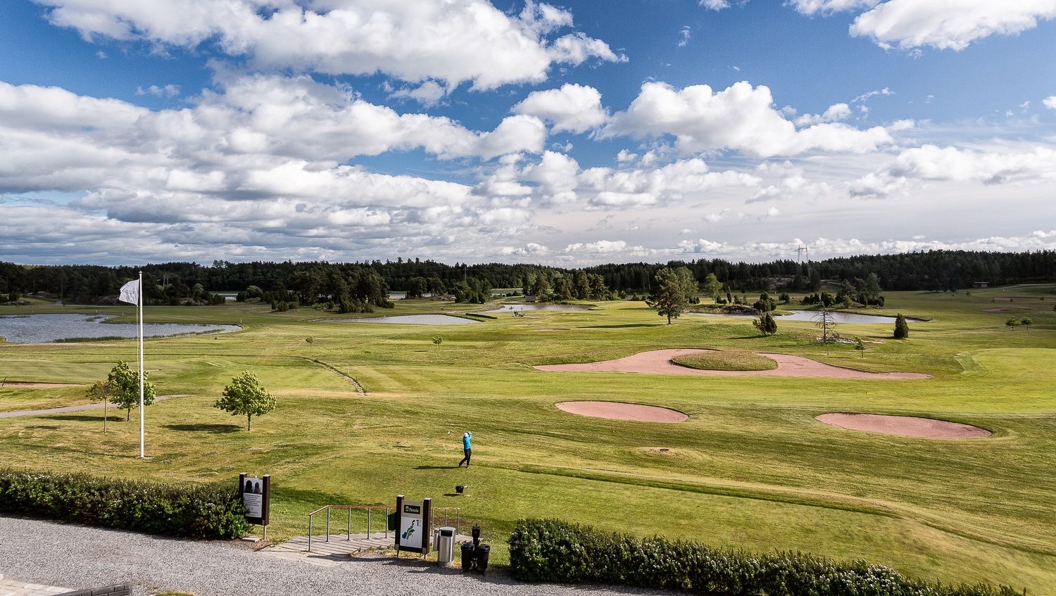 Näkymä Kultarannan vehreälle golf-kentälle, jossa on pelaajia lyömässä. Taivaalla näkyy poutapilviä.