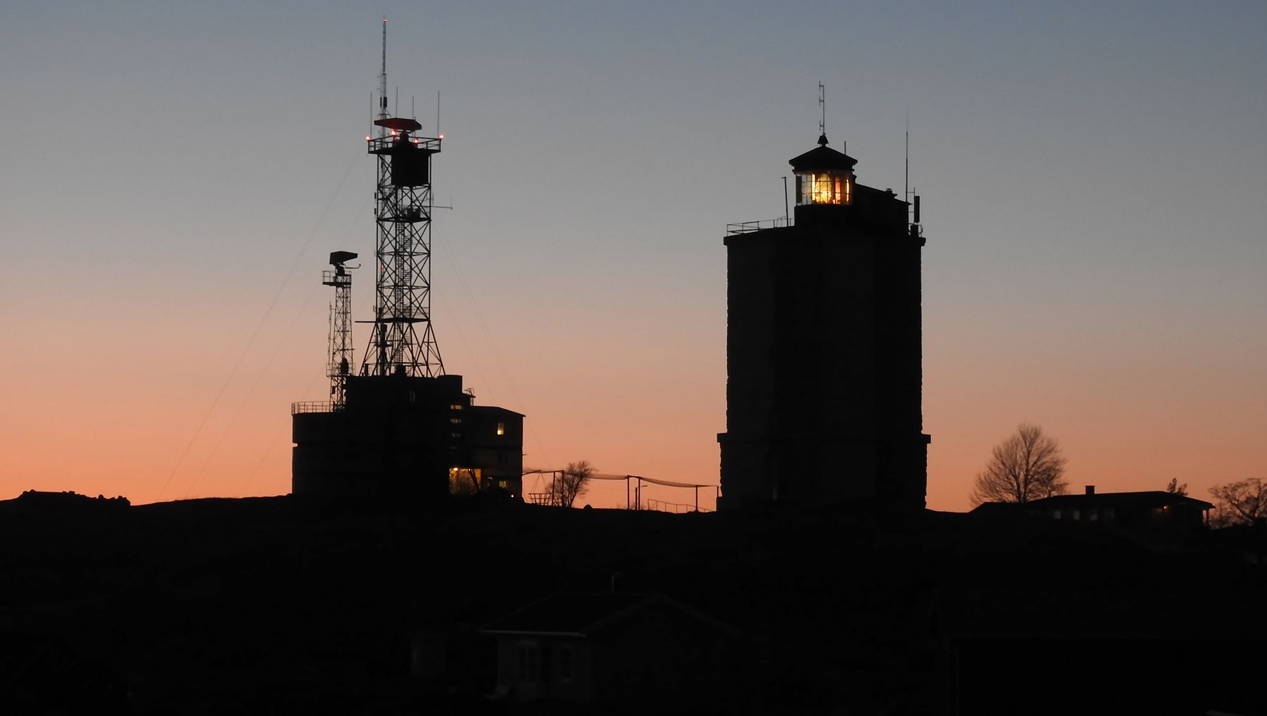 Kuva Utön majakasta auringonlaskun aikaan. Majakka on musta ja taivas on oranssi.