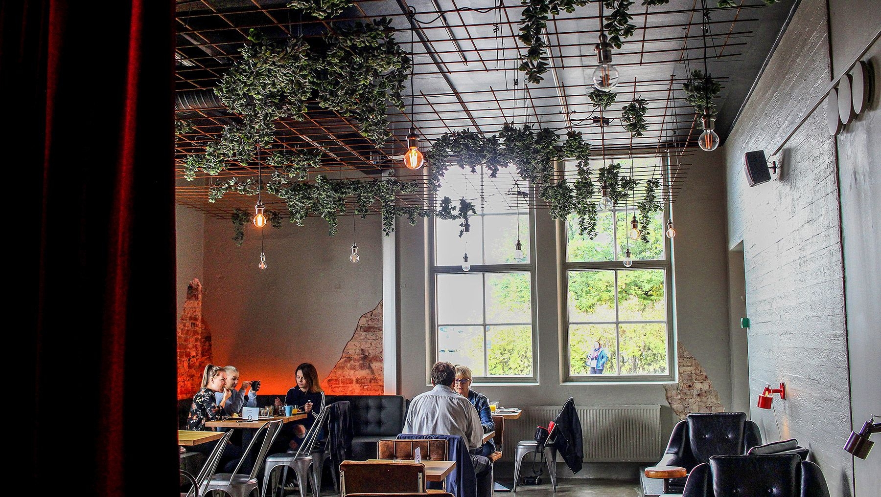 Plants hang from the ceiling at Logomo's restaurant, where diners are enjoying a meal.