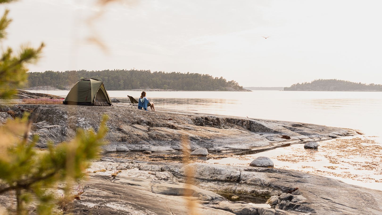 Ett tält och en person på en klippa vid vattnet.