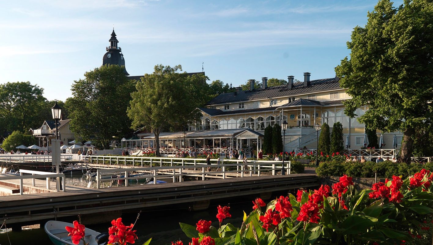 Utsidan av Naantalin Kaivohuone, omgiven av röda blommor och belägen bredvid hamnen.