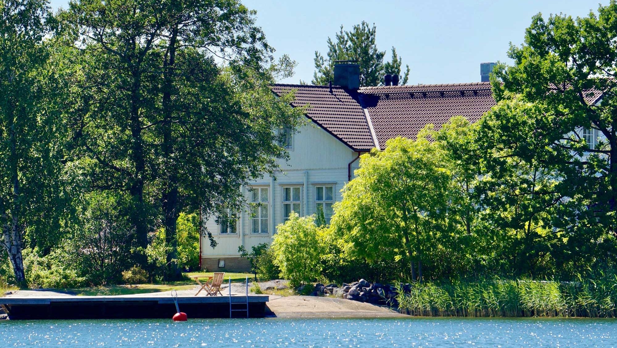 Hyppeis Värdshus vita byggnad, vid havet och omgiven av träd.