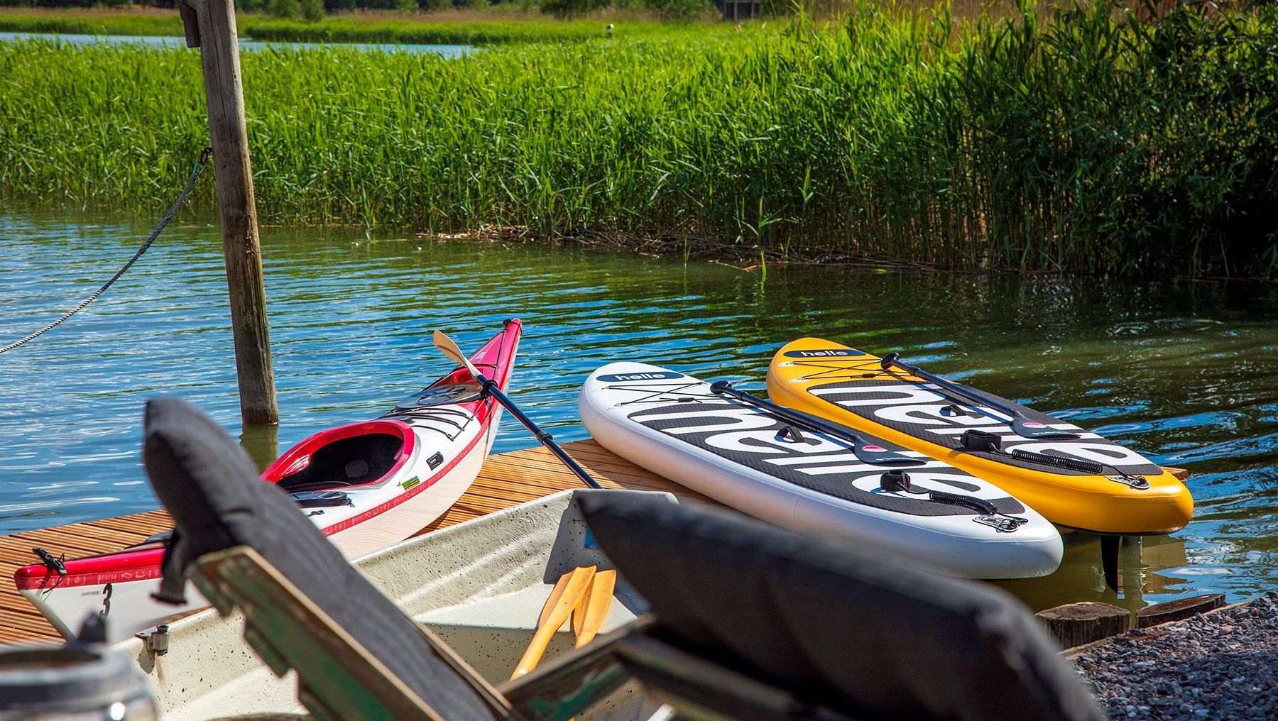 A kayak, two SUP boards and two chairs on a pier.