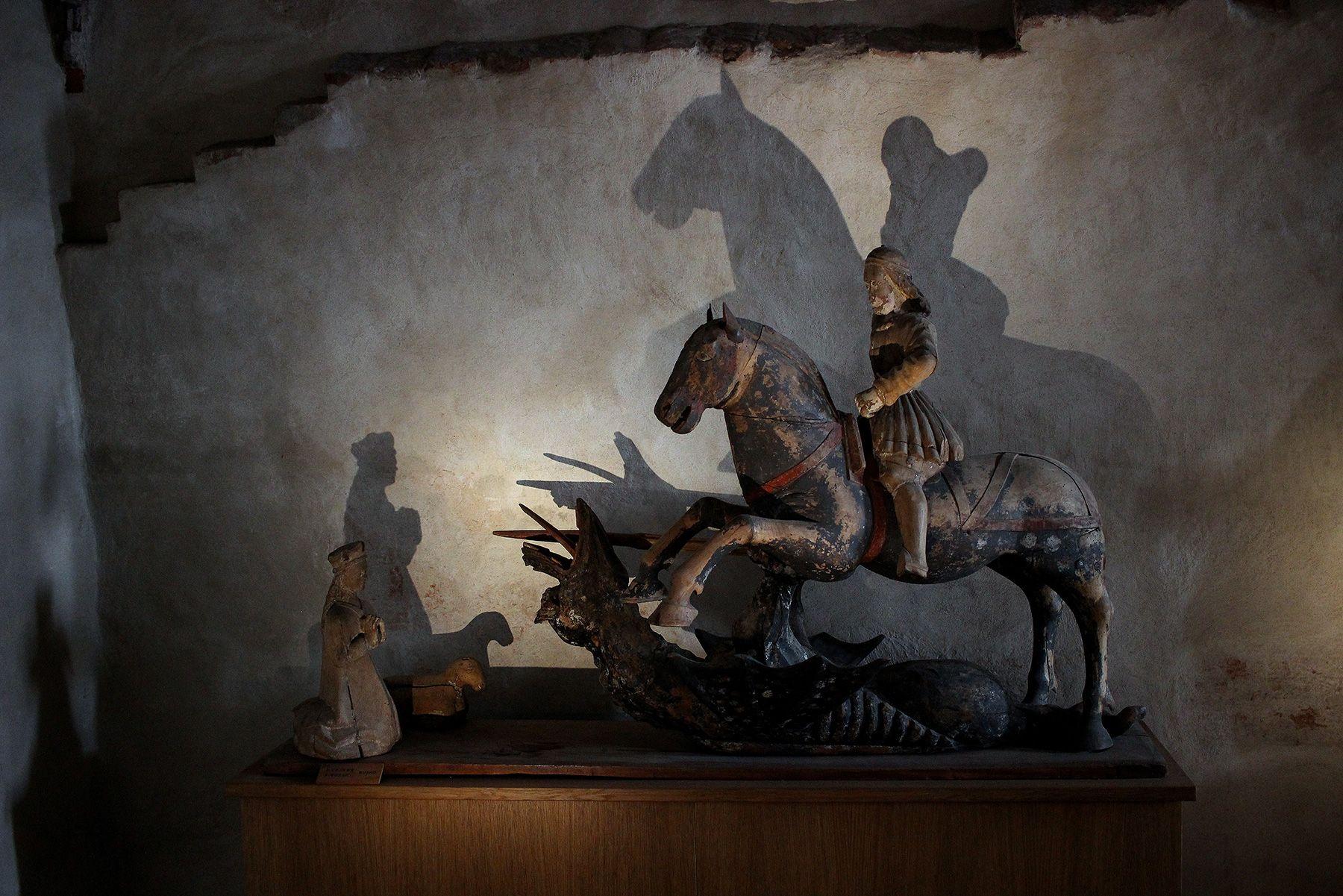 Metallinen pieni patsas, joka esittää laukkaavaa hevosta. Hevosen selässä on ritari ja hevosen edessä on polvillaan hahmo ja lammas.