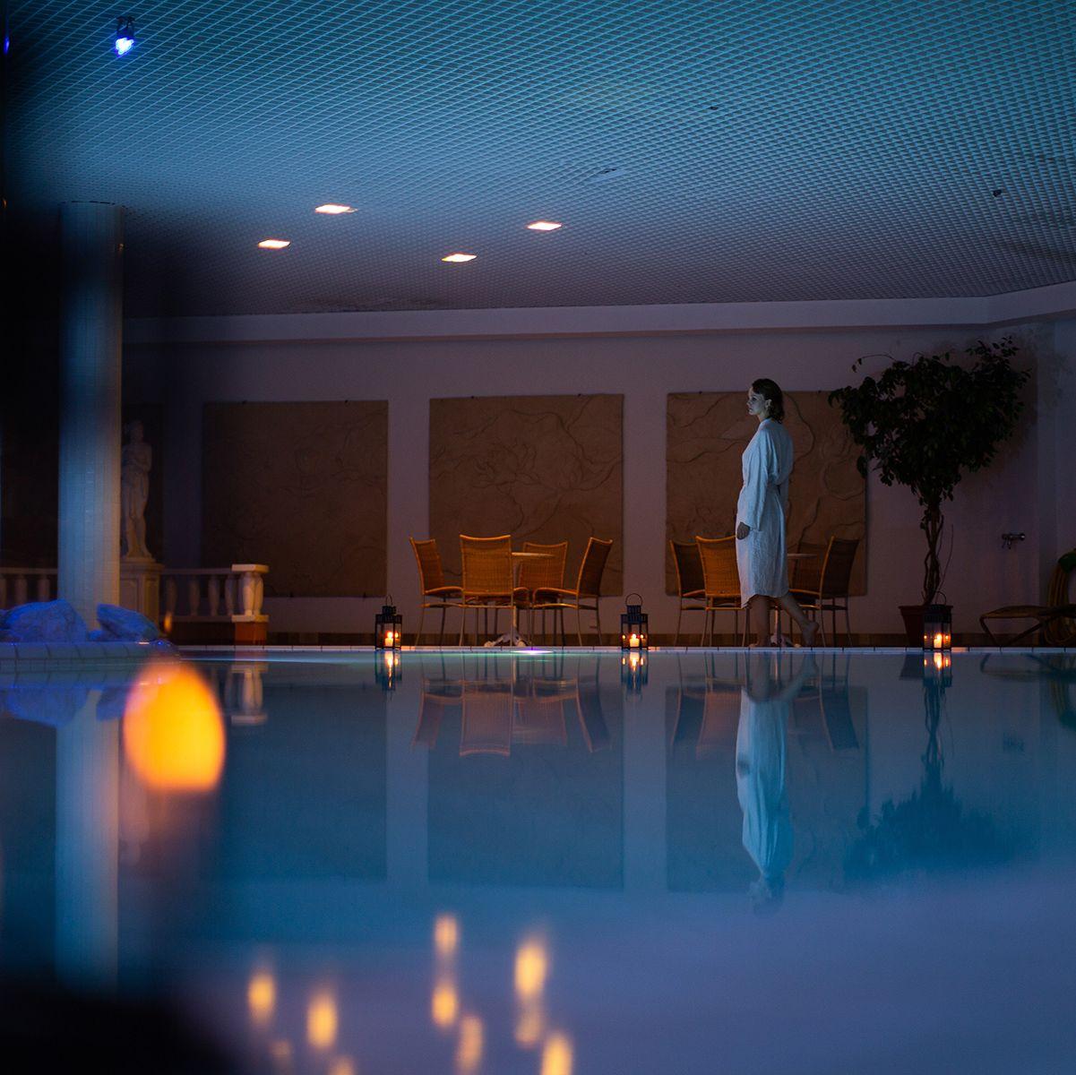 Asiakas kävelee lyhdyin valaistun altaan vieressä valkoinen kylpytakki päällään Naantalin kylpylässä.