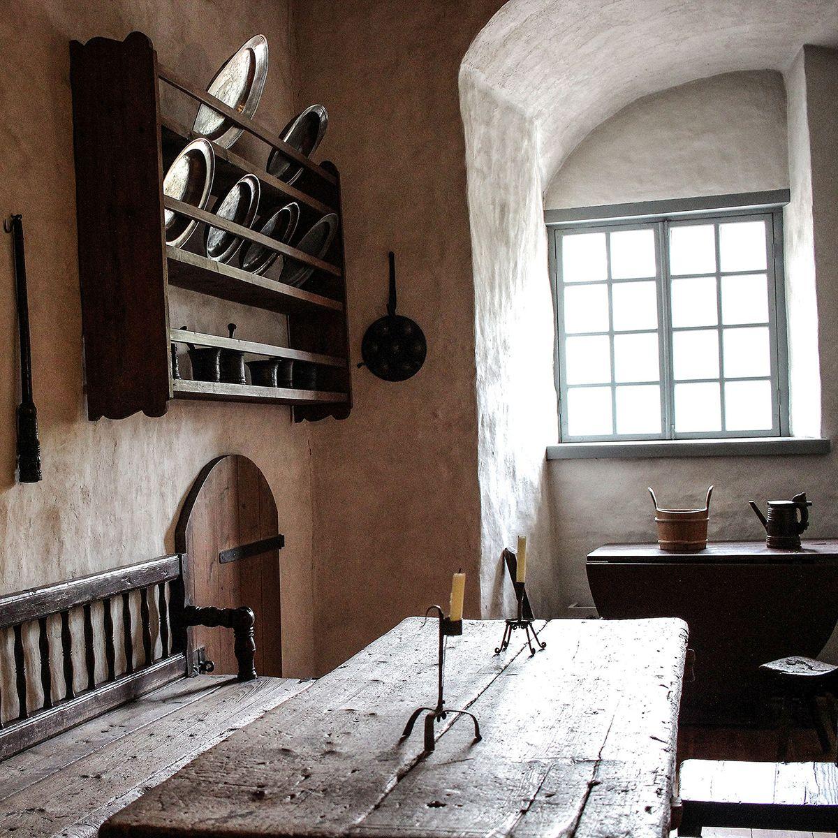 Vanhan keittiön sisustusta Turun linnassa. Keskellä on pitkä lankkupöytä ja seinillä roikkuu kuparisia paistinpannuja ja kattiloita.