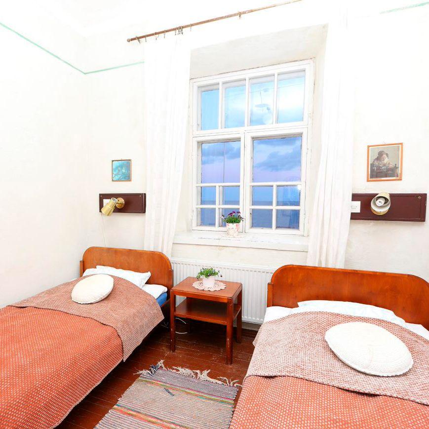 Kahden hengen valkoseinäinen huone Bengstkärin majakassa. Huoneessa on ikkuna ja kaksi sänkyä, joissa on punaiset peitot.