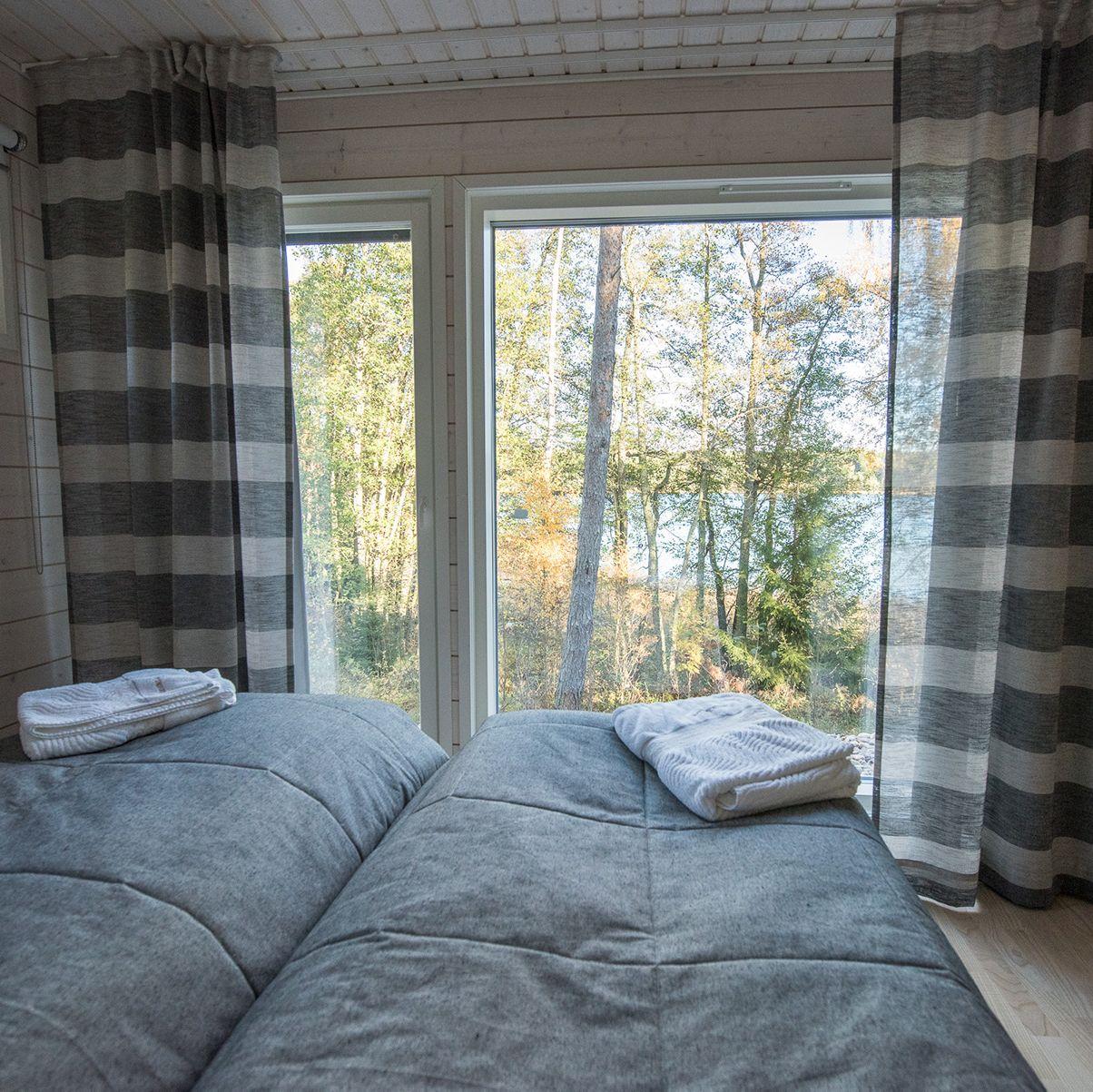 Söderlångvikin kartanon mökkimajoitus. Huoneessa on parisänky, ja ikkunasta avautuu metsämaisema.