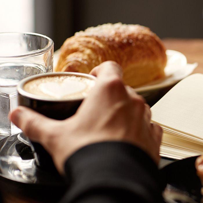 A close-up image featuring the hands of two people, coffees, and baked treats on a table at Ruissalo Spa Hotel.
