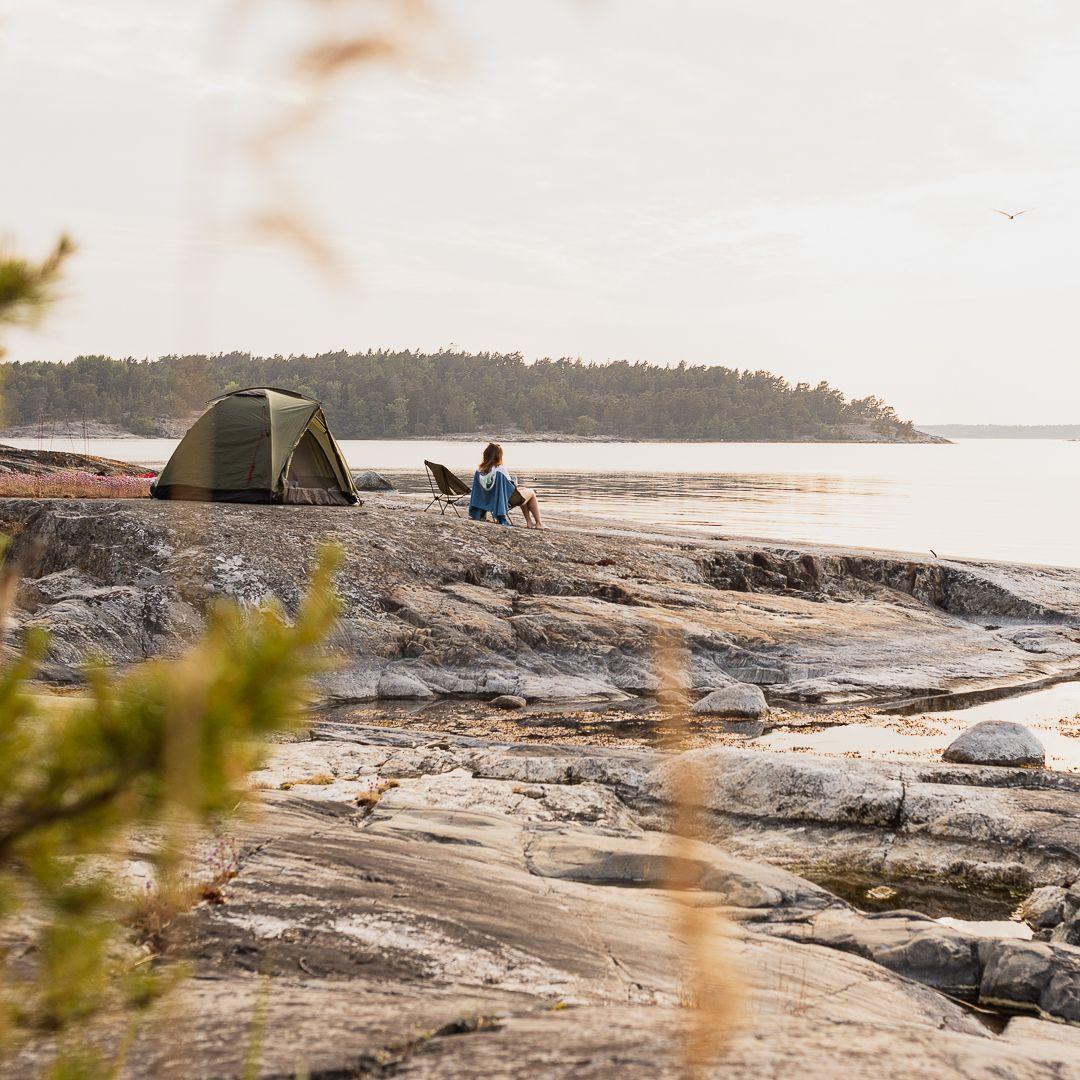 Ett tält och en person på en klippa vid vattnet.