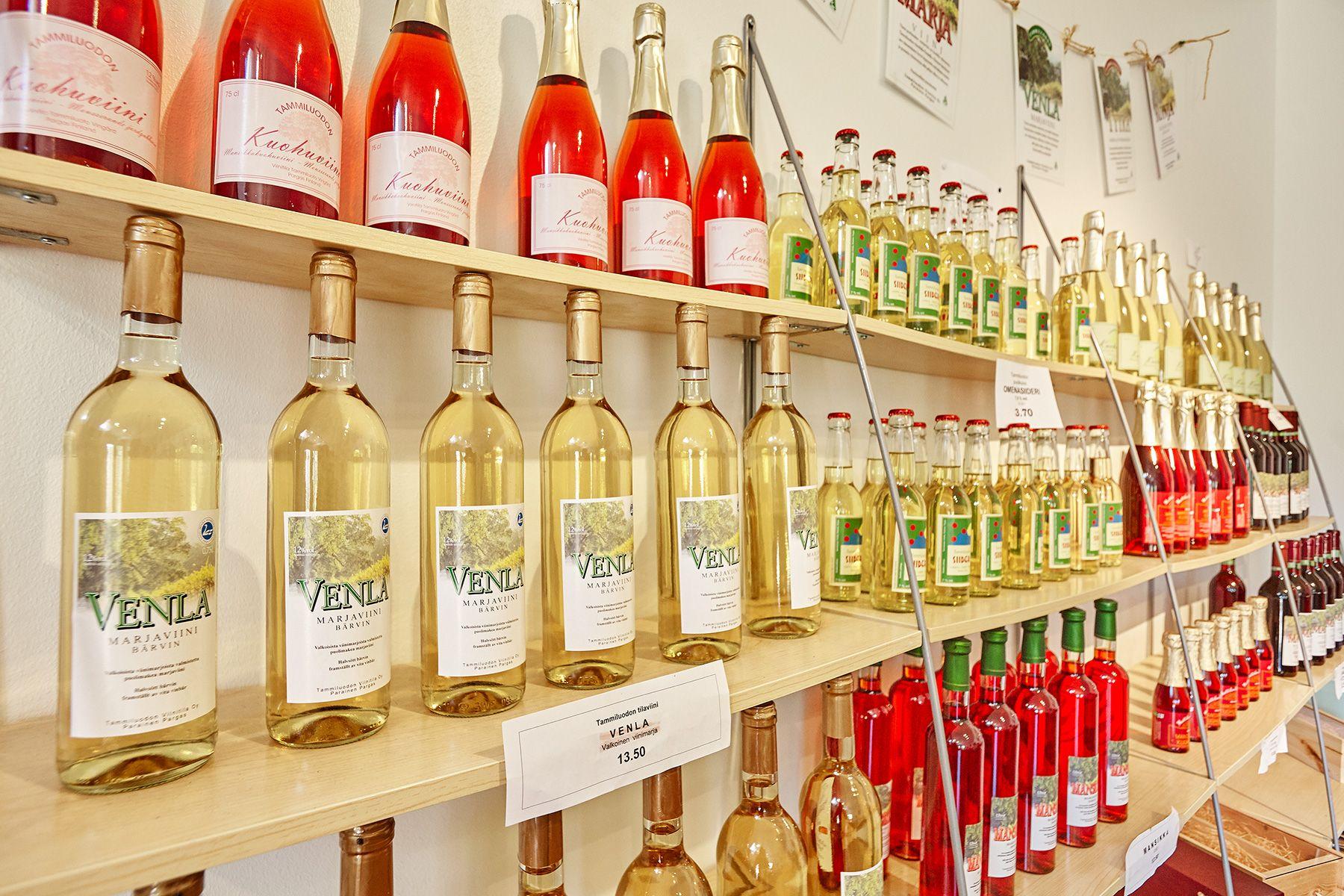 Tammiluodon Viinitilan tuotteita pitkässä kaksikerroksisessa hyllyssä. Pulloissa on punaista ja keltaista juomaa.