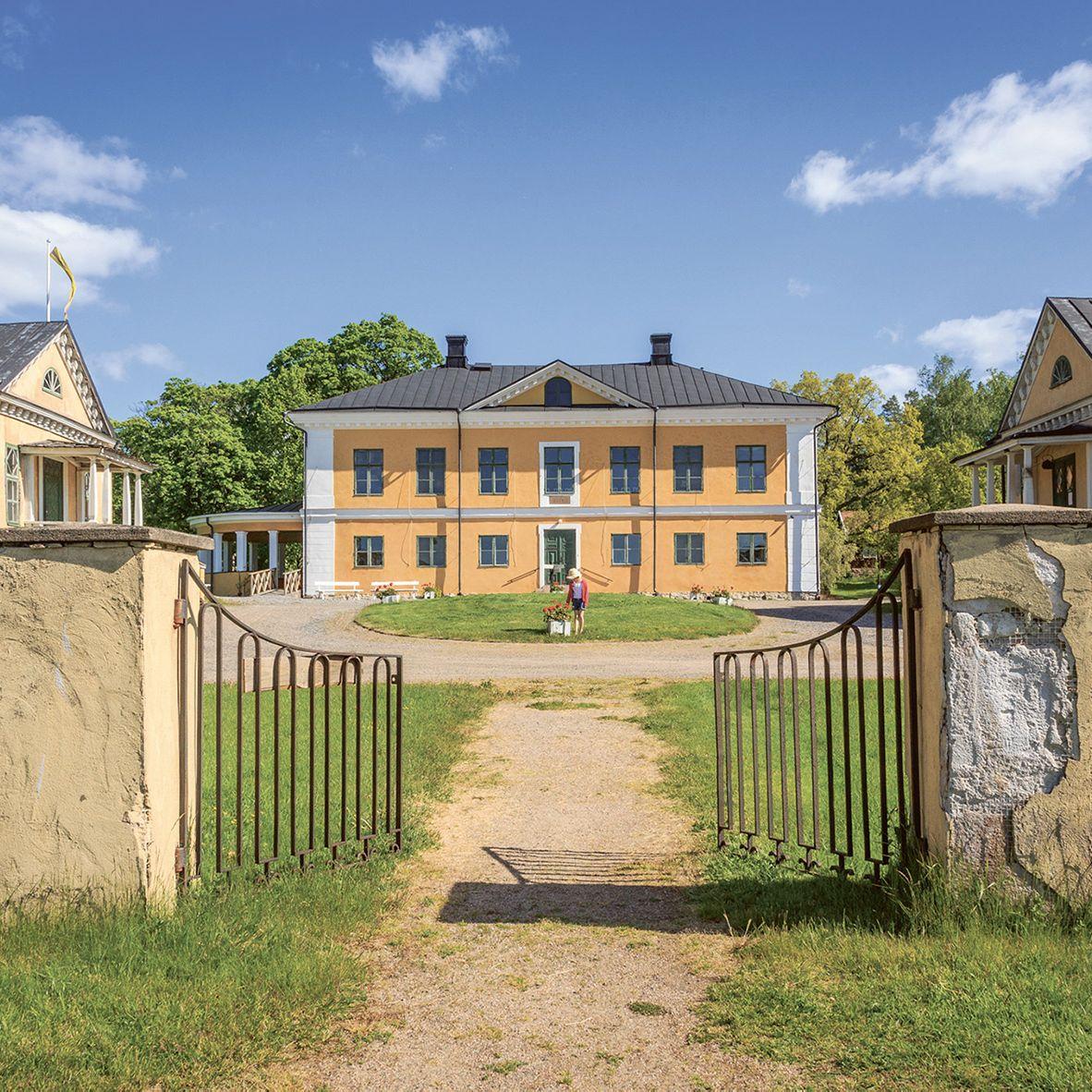 Tre gula byggnader på Brinkhall Manor, bakom en järnport.