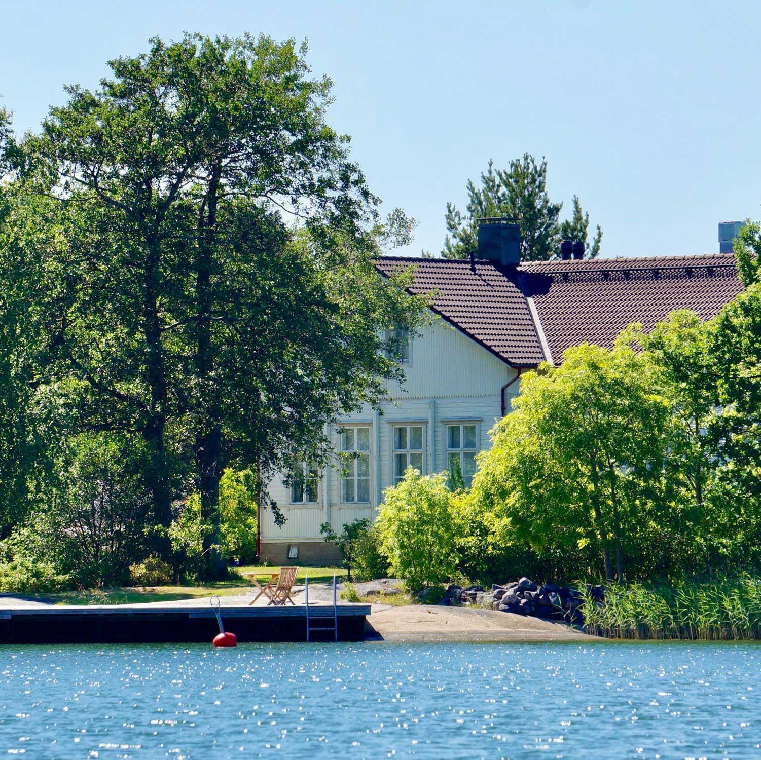 Hyppeis Värdshus vita byggnad, vid havet och omgiven av träd.