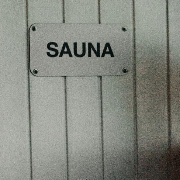 Nainen istuu Mossala Island Resortin saunanrakennuksen edessä. Hänen vieressään on kyltti, jossa lukee ’sauna’.