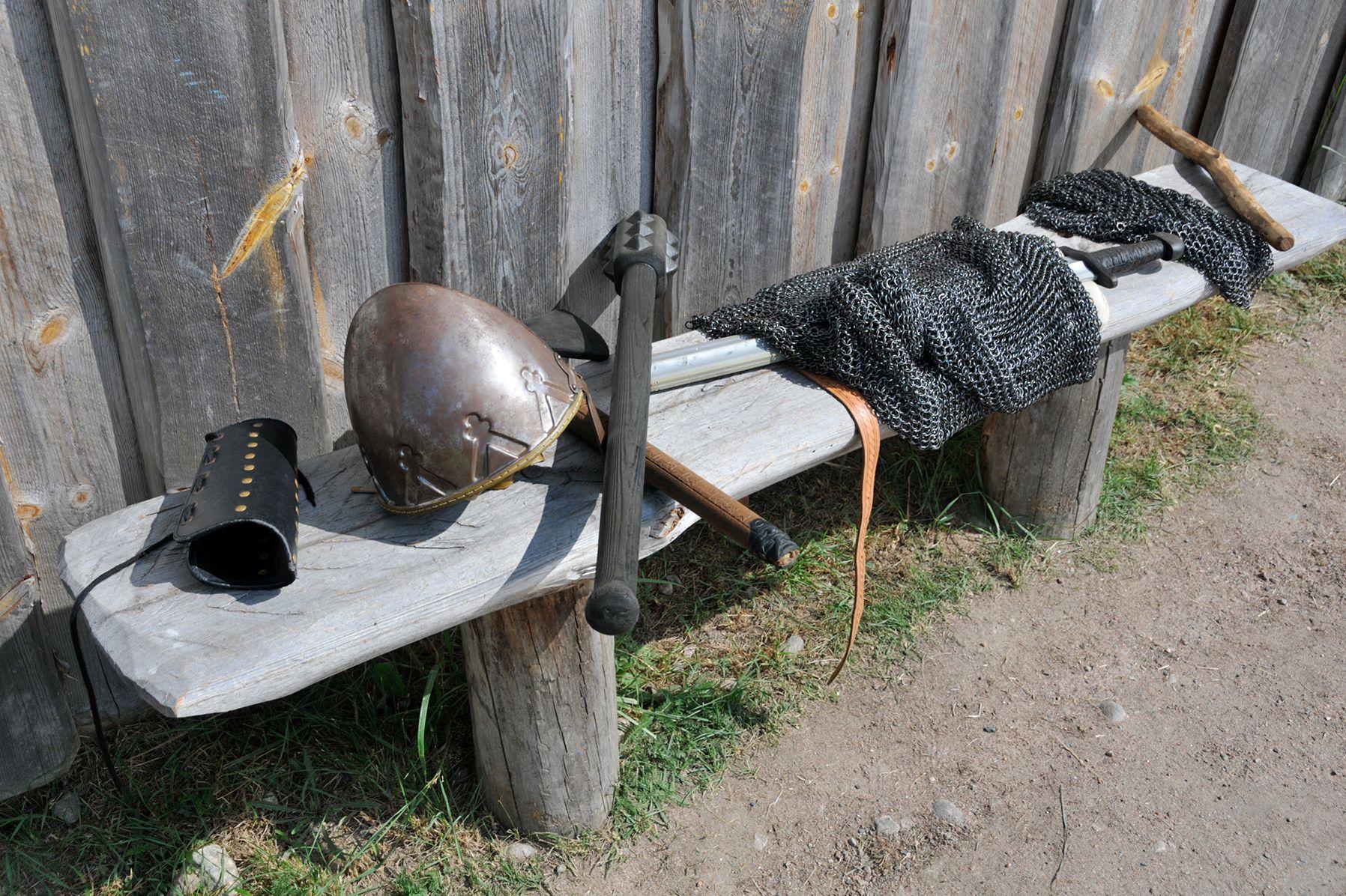 Harmaantuneella puupenkillä pronssinen viikinkikypärä, metallinen rintasuojus ja miekka ja lyömäase.