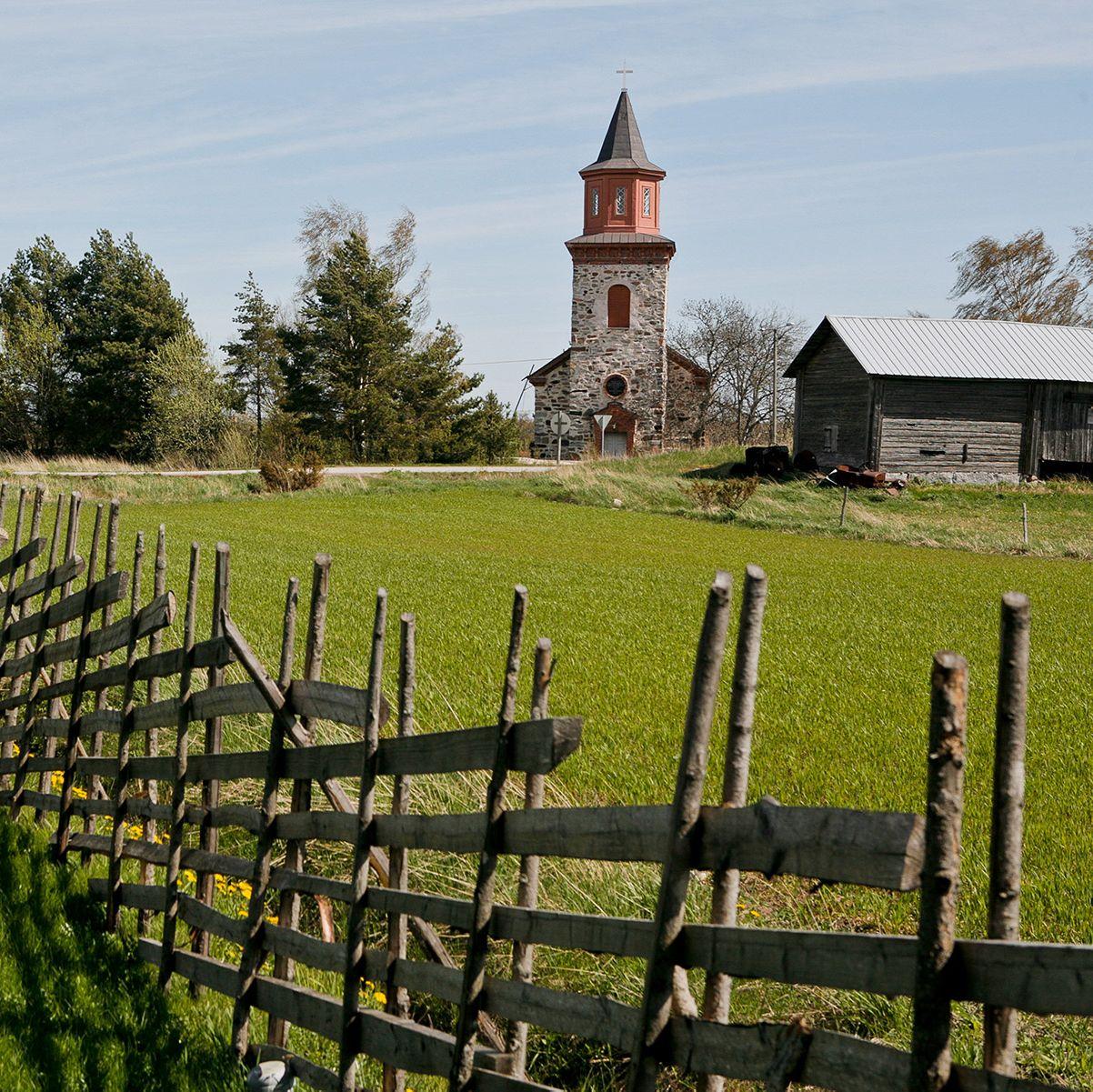 Sofia Wilhelmina kyrka stående högt i ett grönt fält, markerad med ett trästaket.