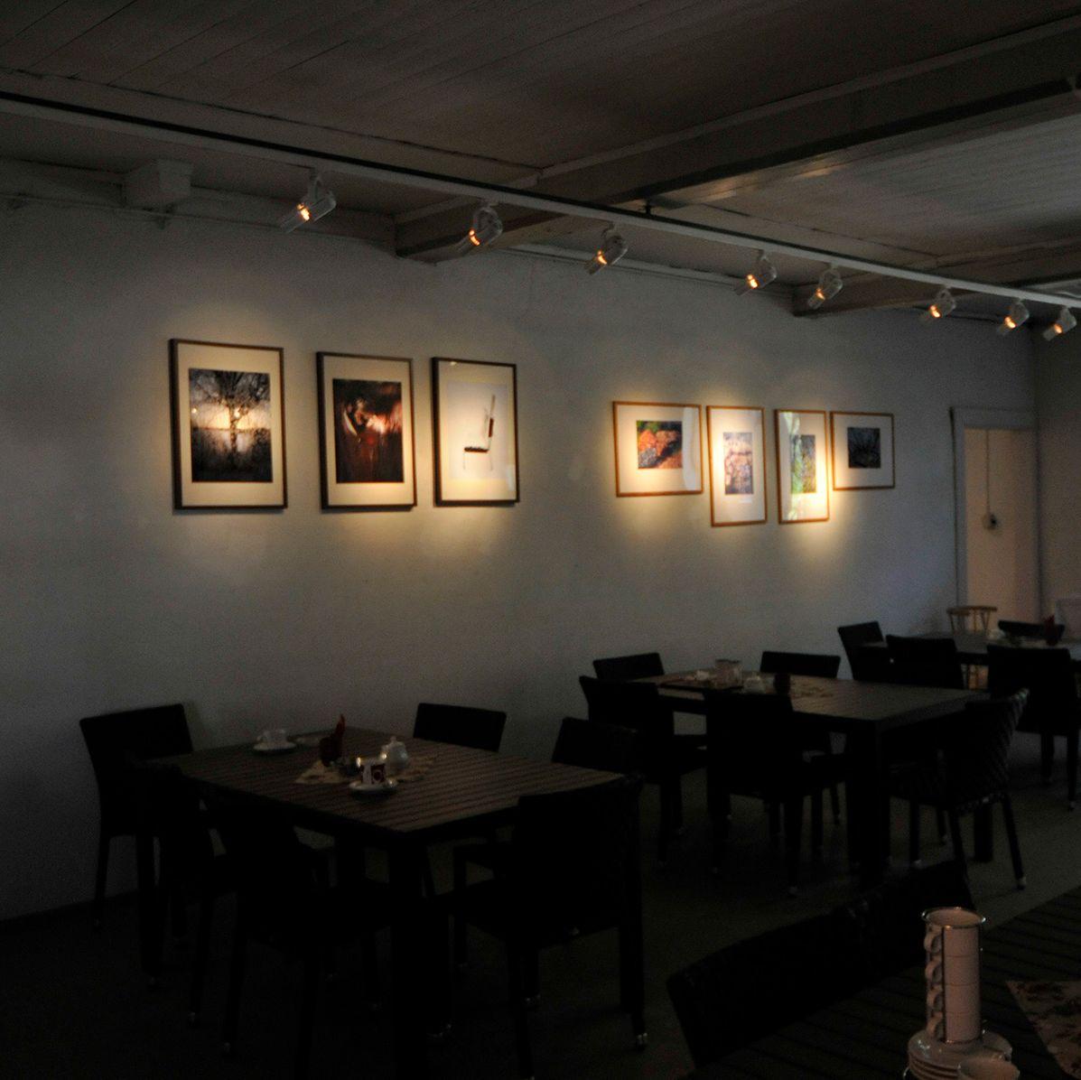 Söderlångvikin kartanon kahvila, jonka seinillä on tauluja. Edustalla on kahvilan pöytiä ja tuoleja.