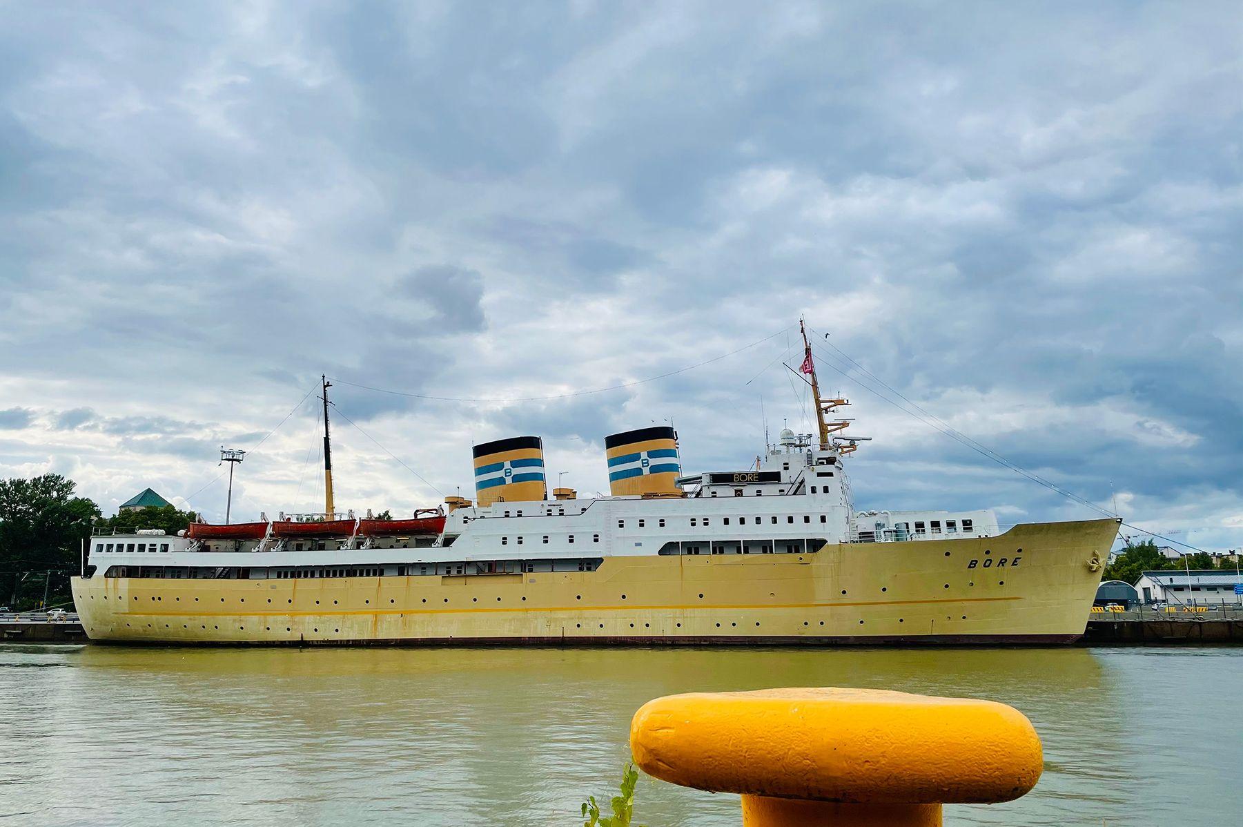 Rahtilaiva joen rannalla ja kuvan etualalla keltainen laivojen kiinnityskohta.